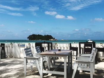 Chairs and table by sea against sky