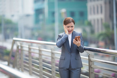 Shocked businesswoman using mobile phone on bridge in city