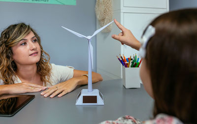Teacher looking windmill while schoolgirl touching blade in ecology classroom