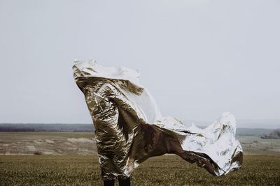 Person wrapped in textile standing on field against clear sky