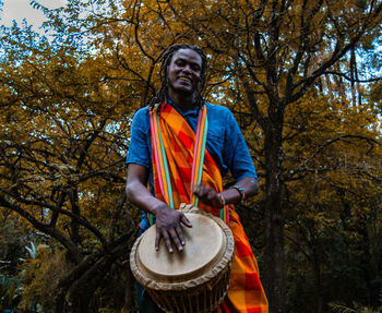 Young man with umbrella standing against trees, kenyan man doing traditional dance masai