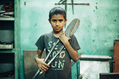 Portrait of boy holding metal standing against wall