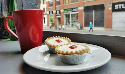 Close-up of coffee with fresh bakewell tarts served in plate at cafe