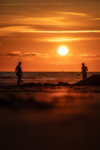 Silhouette man walking at beach against sky during sunset