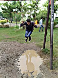 Full length of young man swinging over puddle in park