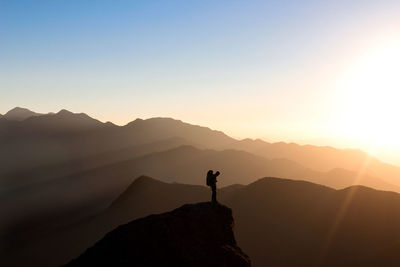 Silhouette man standing on mountain against sky during sunset