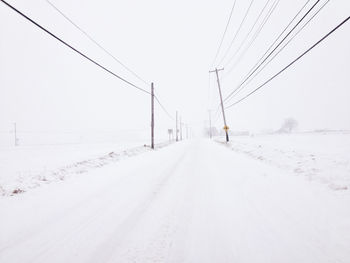 Snow covered road by electricity pylon against sky