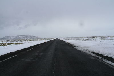 Road amidst snow covered landscape against sky