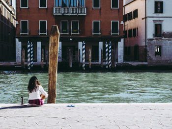 Woman sitting at canal against buildings