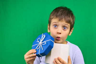 Portrait of boy holding leaf against green background