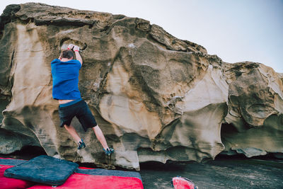 Man climbing on rock formation against sky