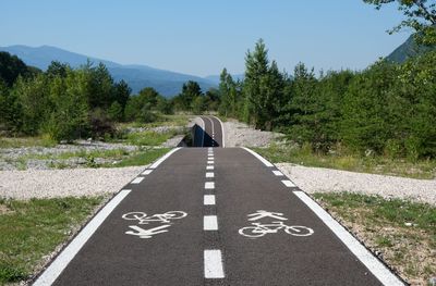 Perspective of a cycle path amidst trees against sky