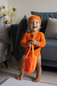 Cute smiling baby standing by sofa at home