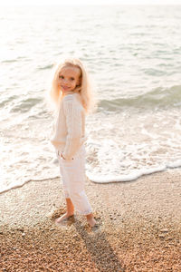 Cute stylish kid girl 5-6 year old wear white knit sweaterand pants rest over sea shore 