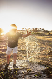 Young boy running under a sprinkler in evening sun