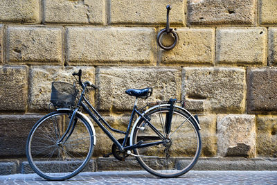 A bicycle leaning against a stone wall with an okd ring used in the past for tie horses, lucca