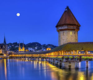 Illuminated building by river against sky at night