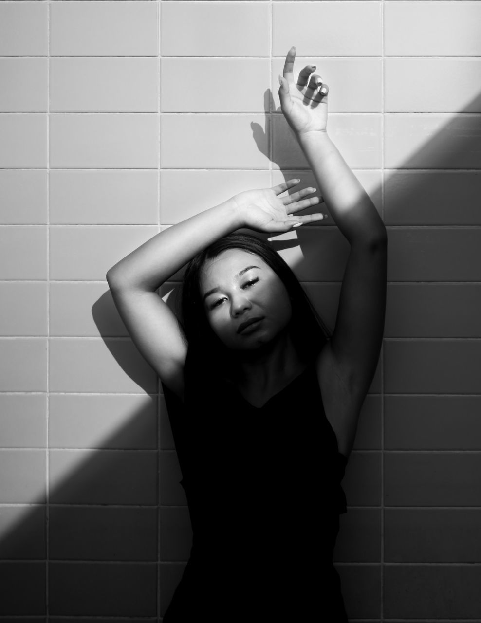 PORTRAIT OF YOUNG WOMAN WITH ARMS RAISED IN BATHROOM