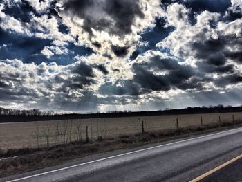 Road passing through field against cloudy sky