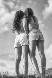 Rear view of women standing on field against sky