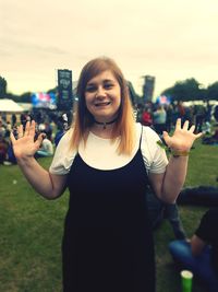 Portrait of smiling woman gesturing while standing on field against sky during festival