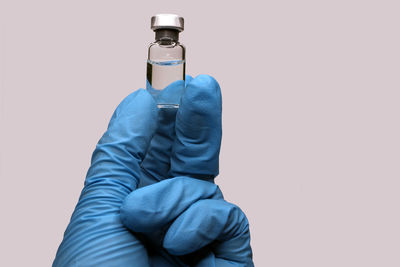 A hand in a blue medical glove close-up holding a vaccine against a light background. 