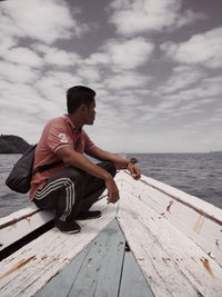 Man sitting on wood by sea against sky