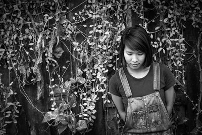 Thoughtful woman standing against creepers growing on wall