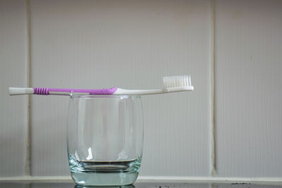Close-up of toothbrush in drinking glass against tiled wall