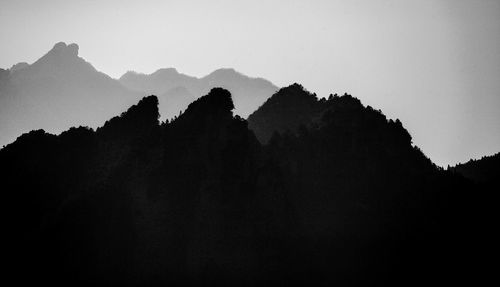 Silhouette trees and mountains against clear sky