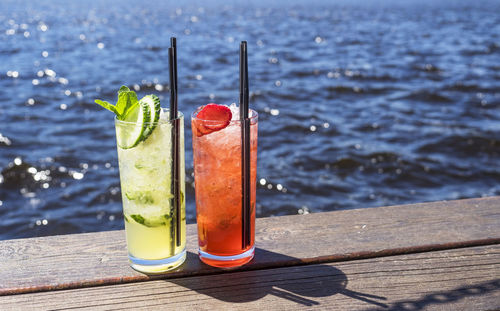 Close-up of drinks on boardwalk against sea