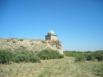 Built structure on field against clear blue sky