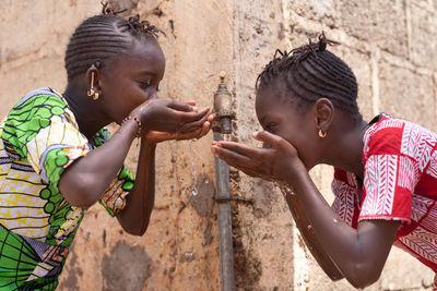 Girls drinking water from faucet against wall