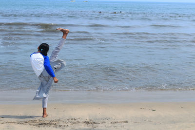 Rear view full length of girl doing martial arts at beach