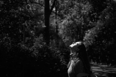 Side view of woman standing against trees in forest