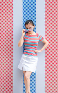 Portrait of woman in sunglasses standing against colorful wall