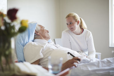 Daughter talking to senior man reclining on hospital bed