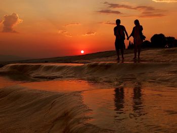People on beach against sky during sunset