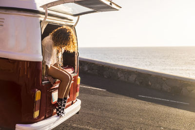 Woman sitting in vehicle on road against sea