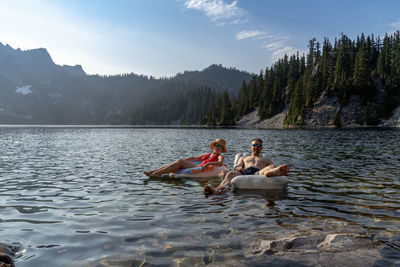 Couple on inflatable rings in lake against sky