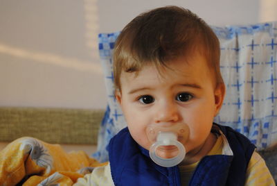 Portrait of cute baby boy with pacifier in mouth sitting at home