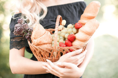 Girl hold basket with food  fresh bread, strawberry, grapes, croissant in park. preparing picnic