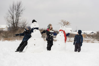 Siblings playing with snowman during winter
