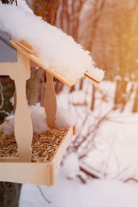 Wooden feeder for wild forest birds with food hanging on tree covered with fresh snow