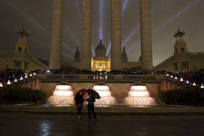 People on street against illuminated buildings at night