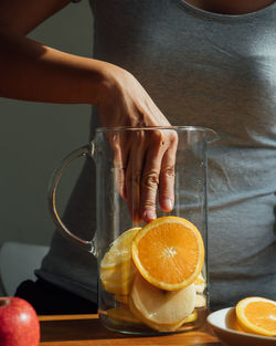 Midsection of woman with orange slices in juicer on table