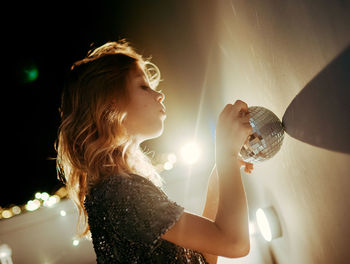 Side view of woman holding illuminated string lights