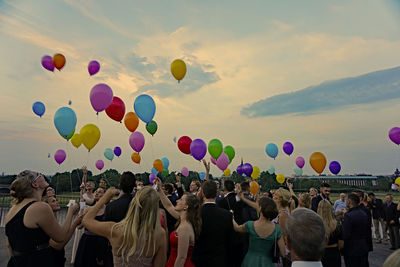 People releasing multi colored balloons at graduation party during sunset