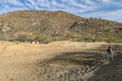 Rear view of people walking on mountain against sky, damm, dam, dry dam, drought, desert