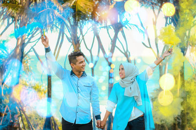 Young couple holding smoke bombs while standing in park